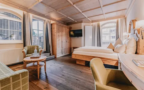 Landleben Gemütliches Hotelzimmer mit Holzmöbeln, Doppelbett, Sitzecke und großen Fenstern